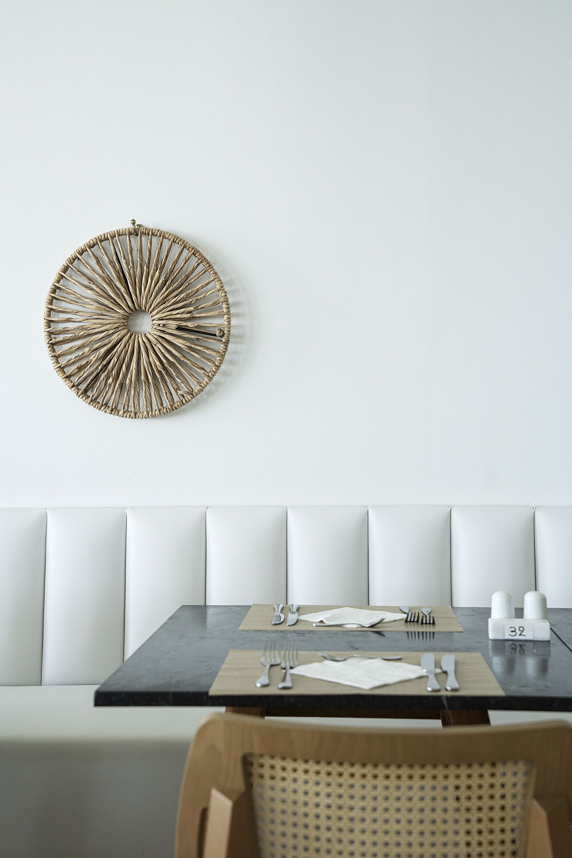A dining area with a round woven wall decor, a black table, and white cushioned seating.
