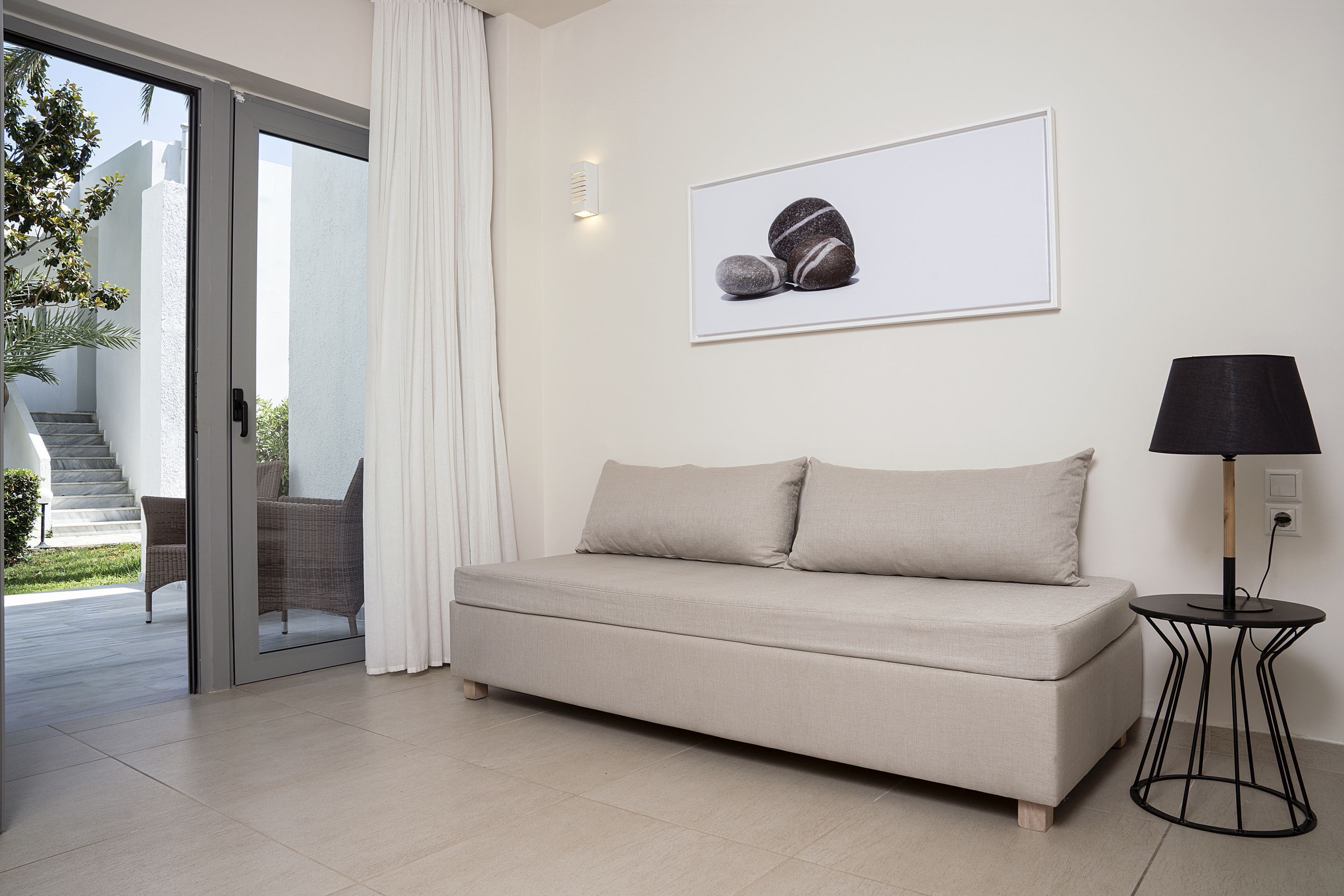 Een moderne woonkamer met een beige bank, een kleine ronde tafel met een lamp, en een lijst met een foto van rotsen aan de muur.