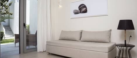 Een moderne woonkamer met een beige bank, een kleine ronde tafel met een lamp, en een lijst met een foto van rotsen aan de muur.