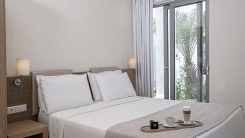 A hotel room with a bed, bedside lamps, a tray with a cup and a small box, and a window with curtains.