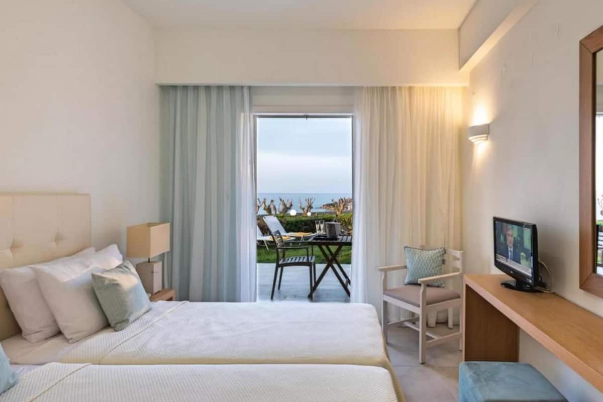 Habitación de hotel con cama, escritorio, televisión y balcón con mesa y sillas.