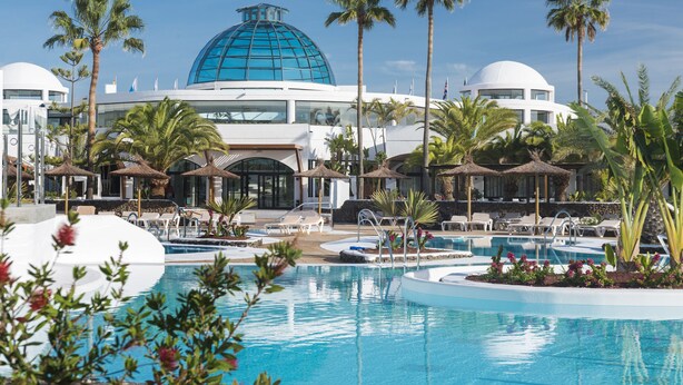 Een resort met een groot zwembad, palmbomen en een opvallend gebouw met een blauwe koepel.