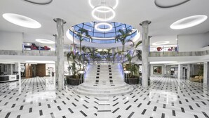 Een ruime lobby met een centrale trap, marmeren vloer en een glazen plafond.
