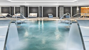 Een modern binnenzwembad met meerdere waterstralen, ligbedden en een wellnessruimte.