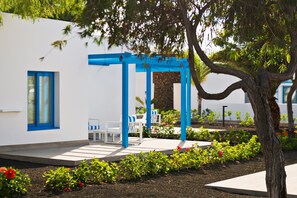 A modern outdoor seating area with white chairs and blue accents, surrounded by well-maintained gardens and a white building with blue trim.