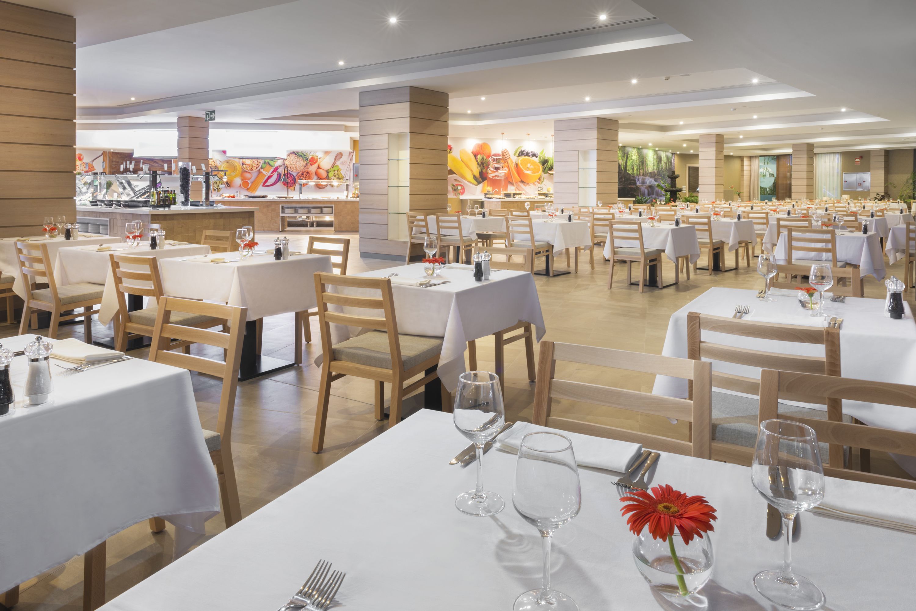 A spacious dining area with multiple tables set for guests, featuring white tablecloths and wooden chairs.