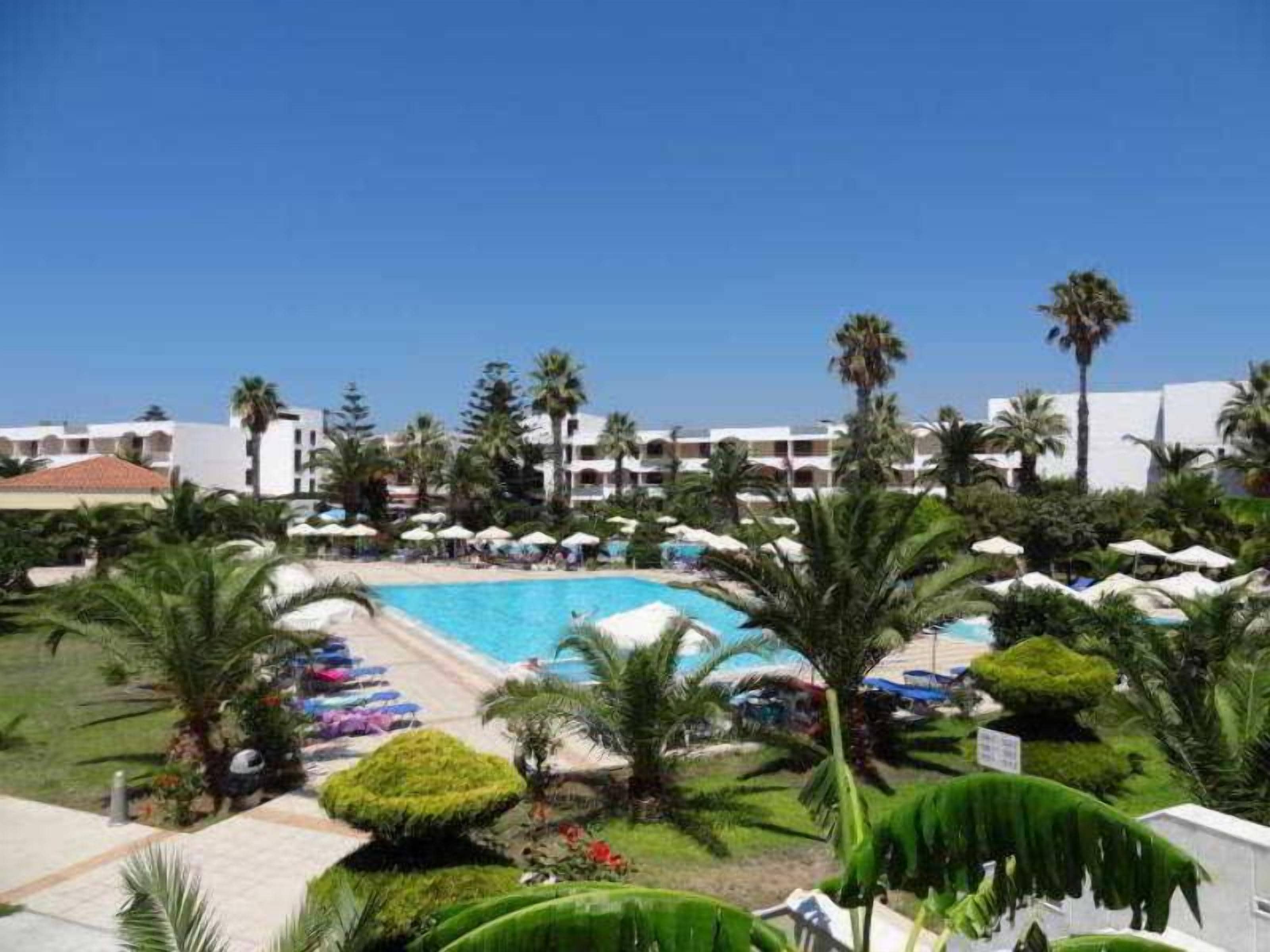 A resort with a swimming pool surrounded by palm trees and umbrellas.