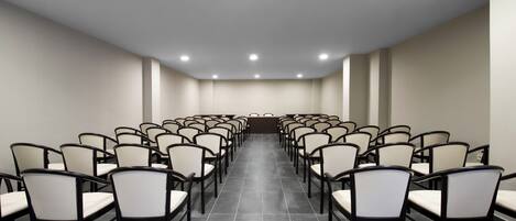 Un salón de conferencias con filas de sillas, piso de baldosas y luces empotradas en el techo.