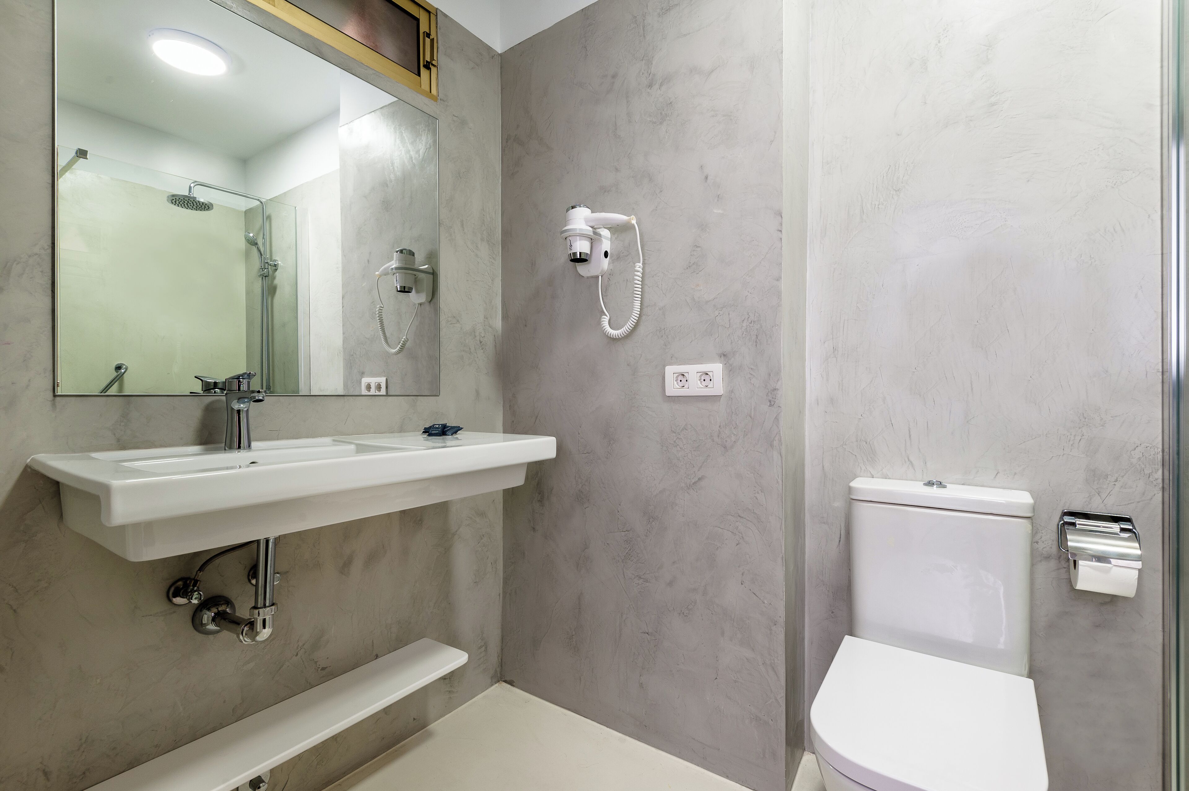 A bathroom with a white sink, mirror, shower, and toilet.