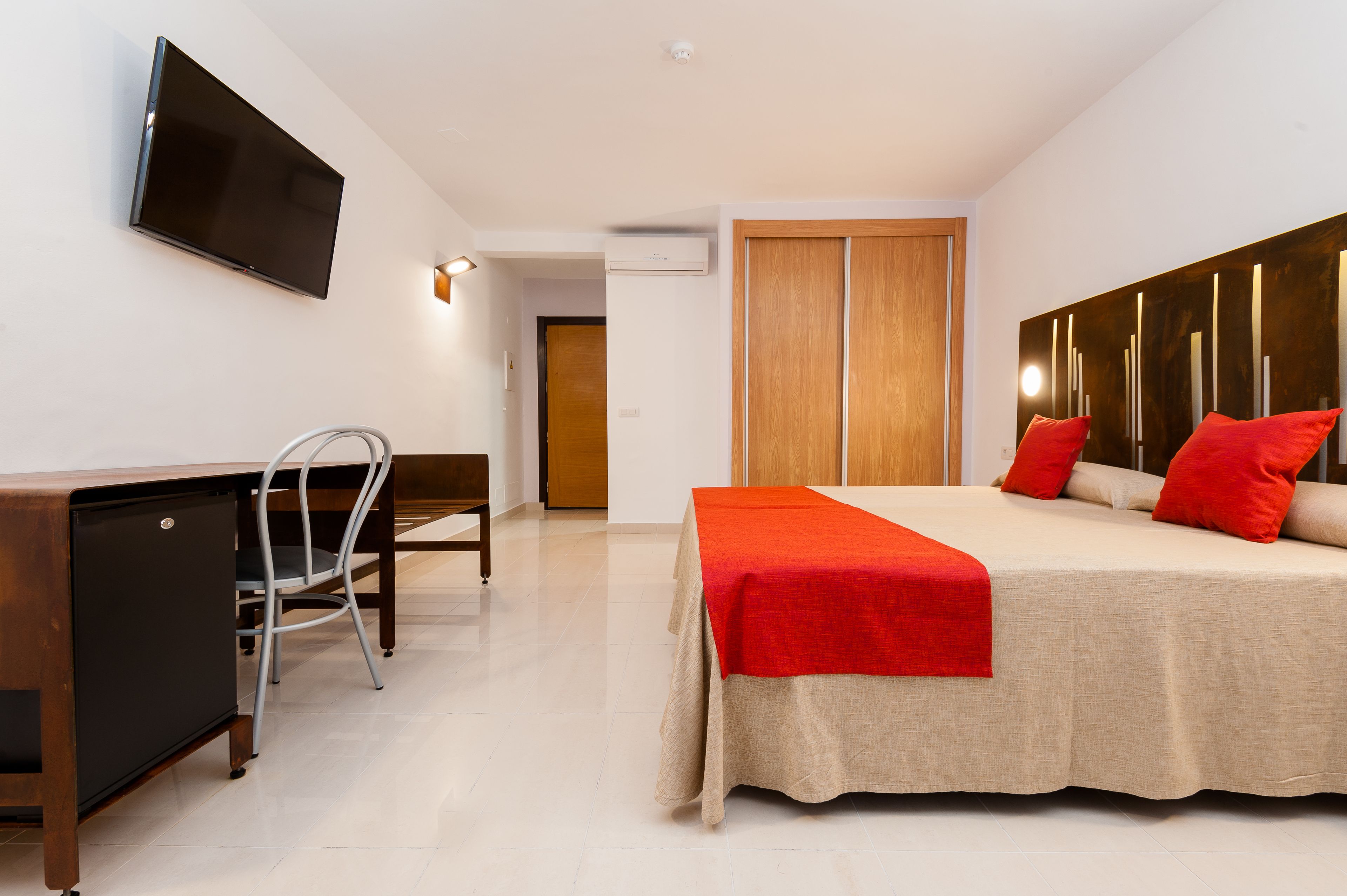 Een moderne hotelkamer met een bed, bureau, stoel en een aan de muur bevestigde televisie.