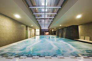 A large indoor swimming pool with a glass ceiling, tiled walls, and a view of the sky. - Kn Aparthotel Columbus (Arona)