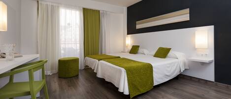 A hotel room with two beds, a desk, a chair, and a bedside table with lamps.