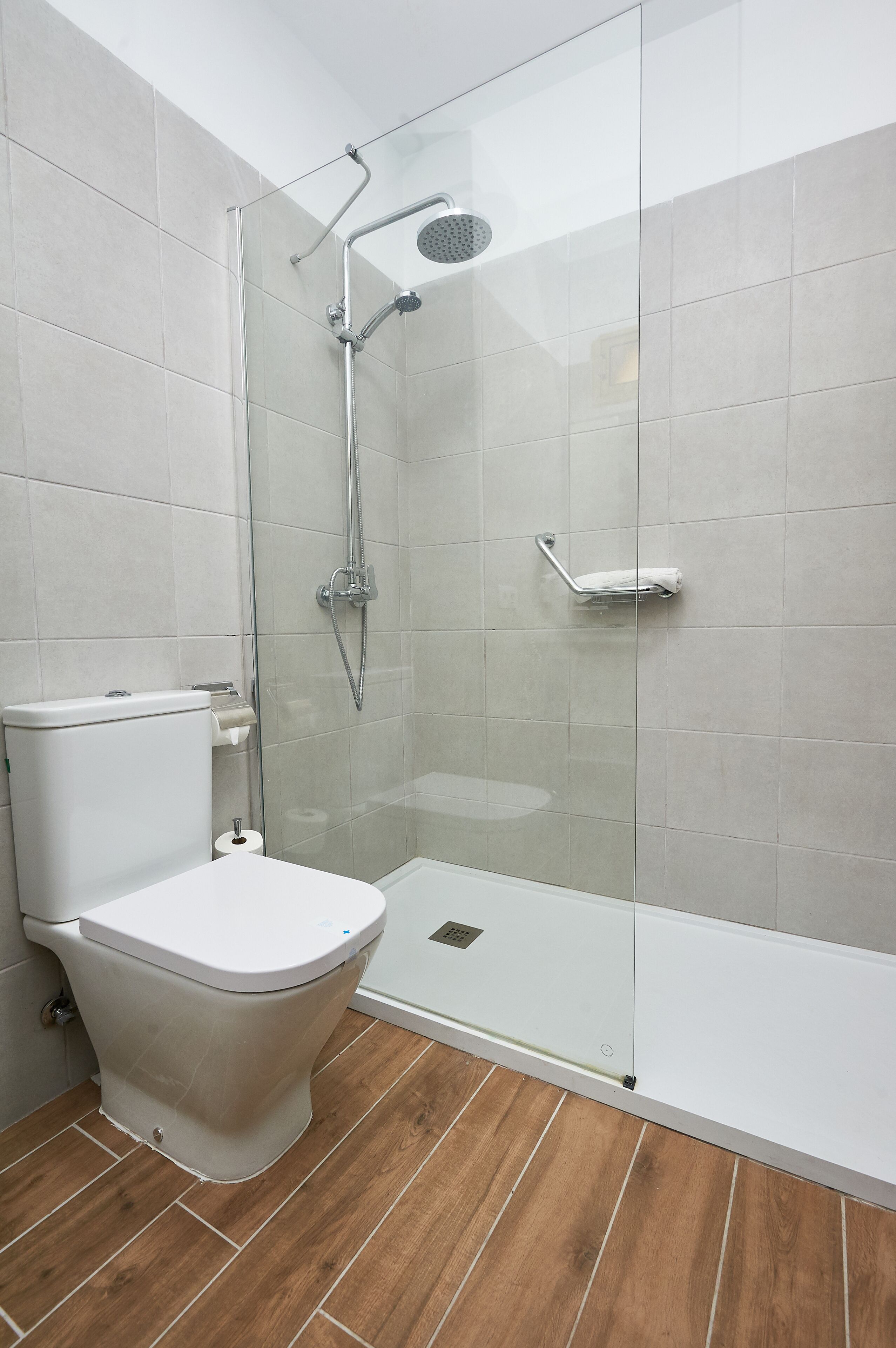 A modern bathroom with a glass-enclosed shower, a white toilet, and a wooden floor.