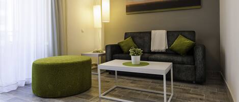 A modern living room with a grey sofa, a white coffee table, a green ottoman, and a painting on the wall.