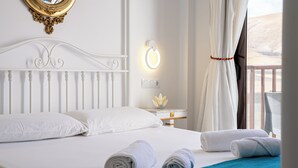 Quarto de hotel com cama branca, almofadas brancas, colcha verde-água e toalhas dobradas sobre a cama.