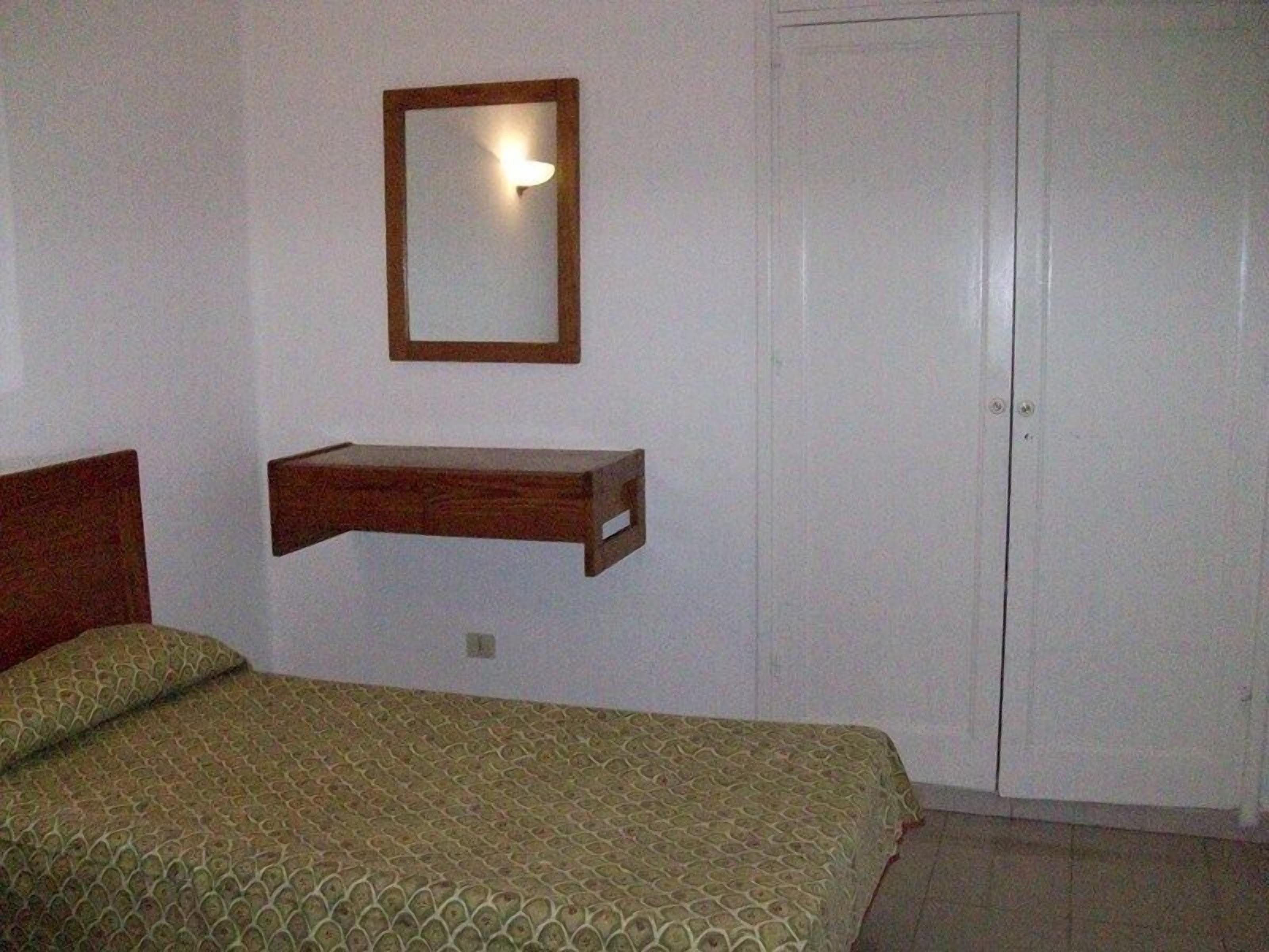 Una camera da letto con un letto, uno scaffale in legno, uno specchio e una porta bianca.