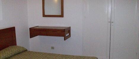 Una camera da letto con un letto, uno scaffale in legno, uno specchio e una porta bianca.
