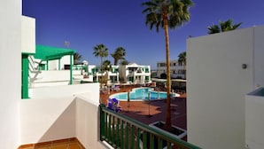 Un patio de hotel con piscina, palmeras y una estructura con techo verde.