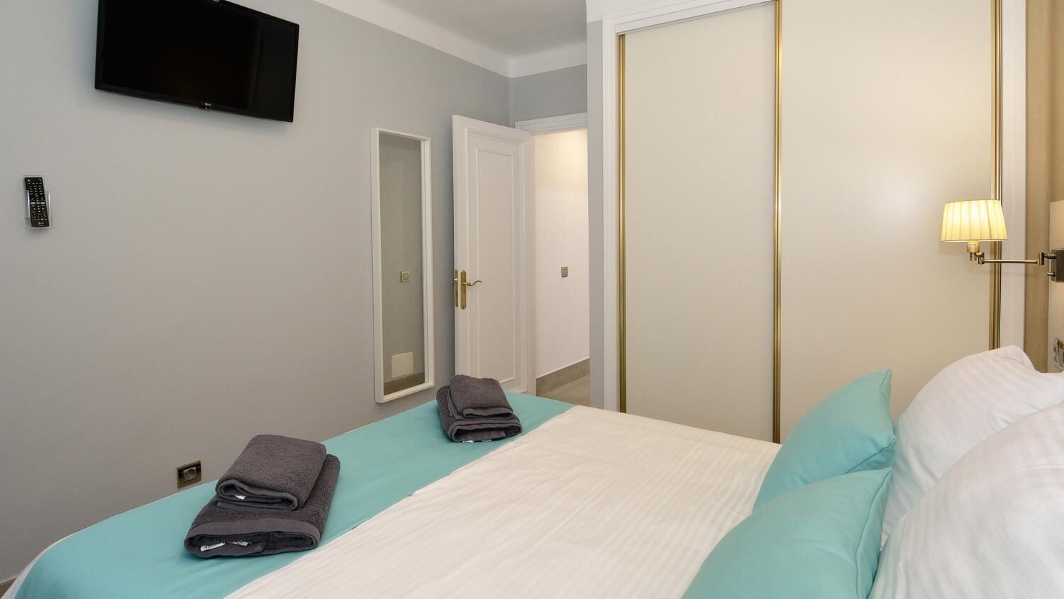 Ein Hotelzimmer mit einem Bett, zwei Handtüchern, einem Fernseher, einer Lampe und einer Tür.