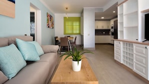 Una sala de estar moderna con un sofá, una mesa de centro con una planta, un comedor con sillas y una cocina con armarios y electrodomésticos.