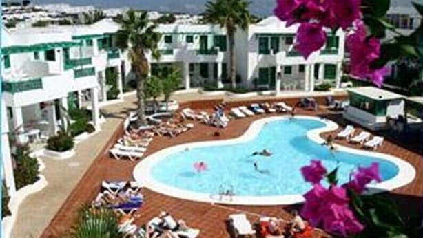Un resort con piscina rodeada de sillones de descanso y palmeras.