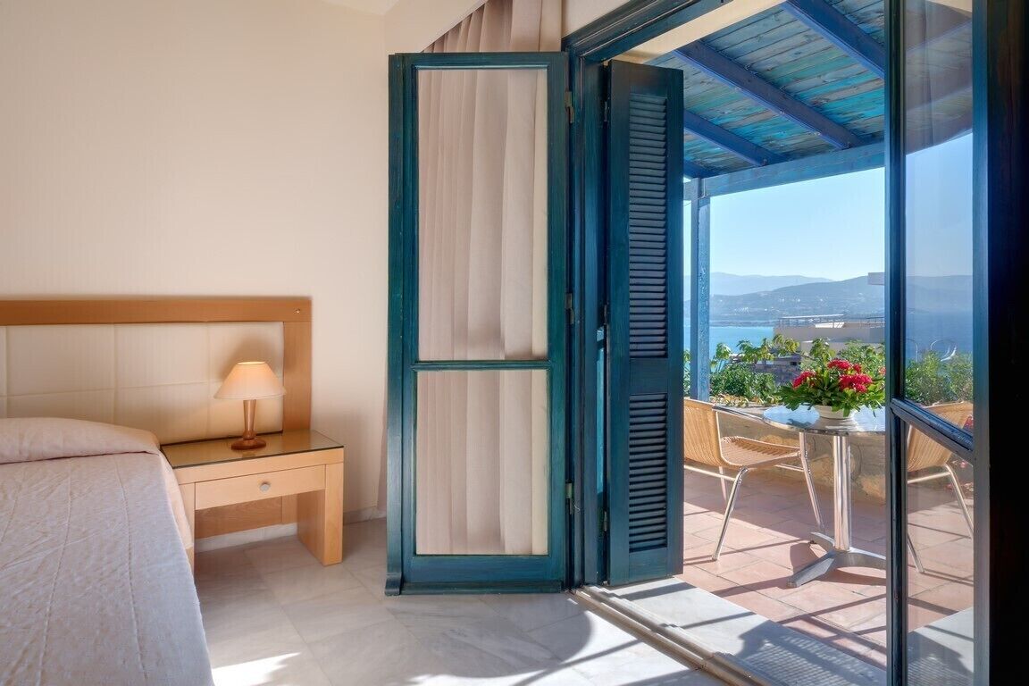 A bedroom with a bed, bedside table, and a view of a balcony with a table and flowers.