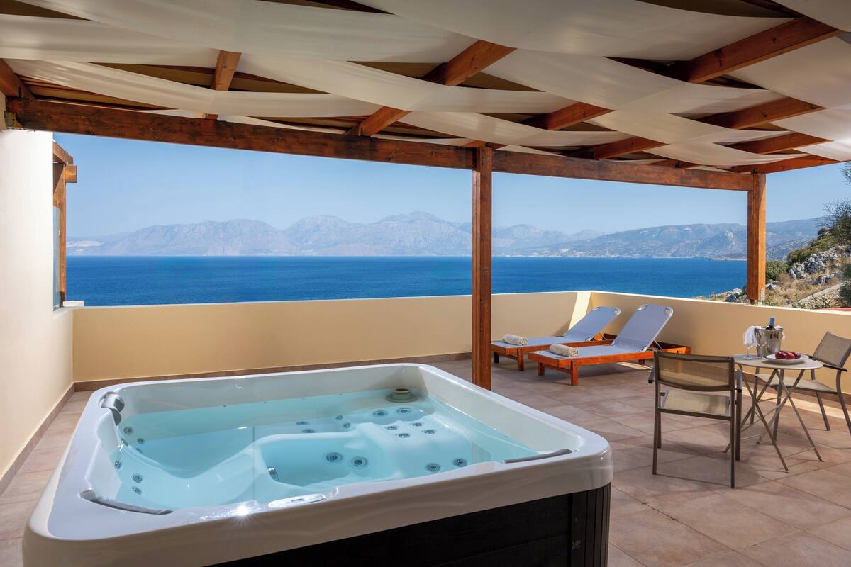 A balcony with a hot tub, lounge chairs, and a view of the sea and mountains.