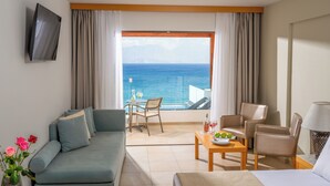 Une chambre d’hôtel avec un balcon, un canapé, une table avec une bouteille et des verres, et un téléviseur fixé au mur.