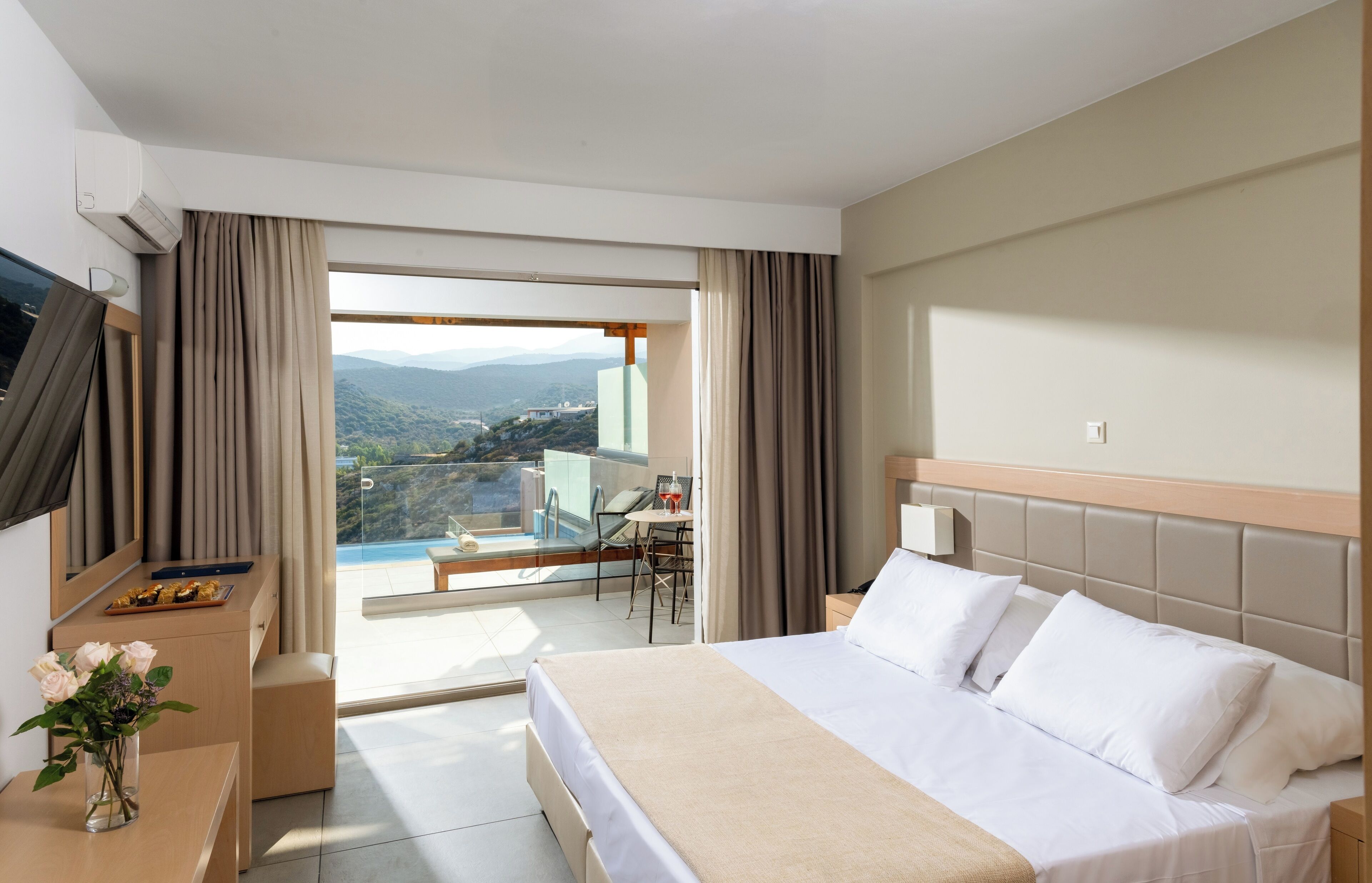 Camera d'albergo con un letto grande, una scrivania con una sedia, un tavolino con una bevanda e vista sulle montagne dalla finestra.