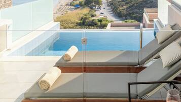 A modern outdoor lounge area with a pool, a glass balustrade, and a view of a coastal town and hills.