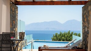 Un balcon avec une piscine, des chaises longues et une table offrant une vue sur la mer et les montagnes.