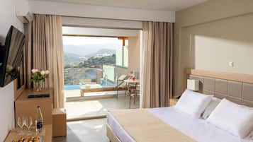 Habitación de hotel con una cama, un escritorio con silla, una mesita con una botella y vasos, y vistas a una piscina y montañas.