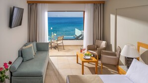 Une chambre d’hôtel avec un balcon, un canapé, un lit, une table avec des fruits et un téléviseur fixé au mur.