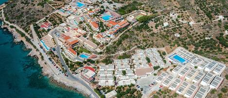 An aerial view of a coastal resort with multiple buildings, a beach, and a large swimming pool complex.