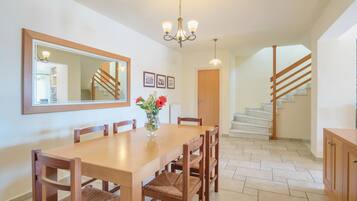 A dining area with a wooden table and chairs, a chandelier, and a staircase in the background.