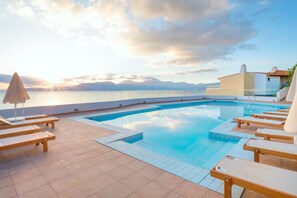 A swimming pool with sun loungers and a view of the sea and mountains.