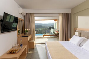 Habitación de hotel con cama, televisión, escritorio con ordenador portátil, silla y vistas a un paisaje montañoso.