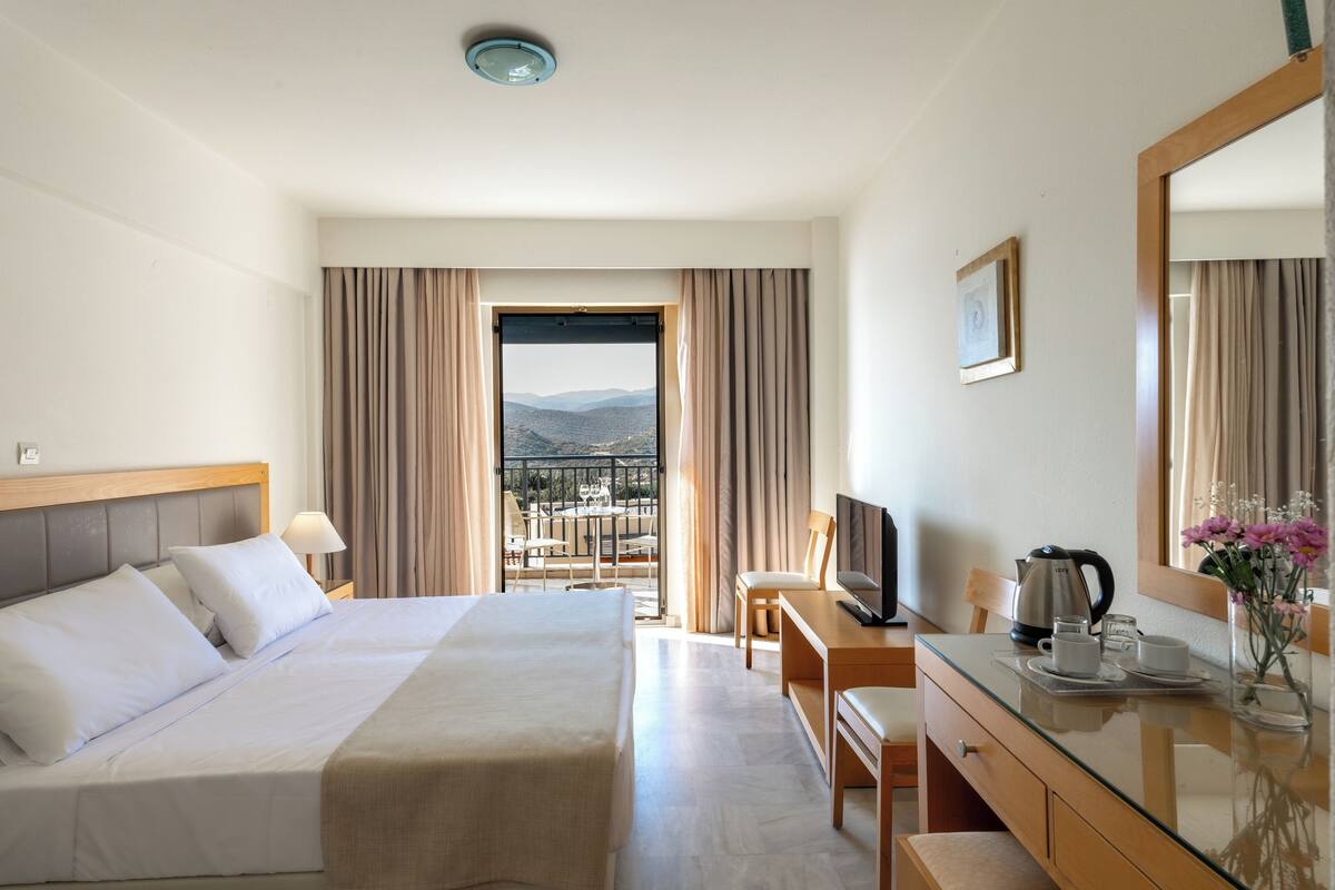 A hotel room with a bed, a desk, a chair, a television, a coffee maker, and a view of the mountains.