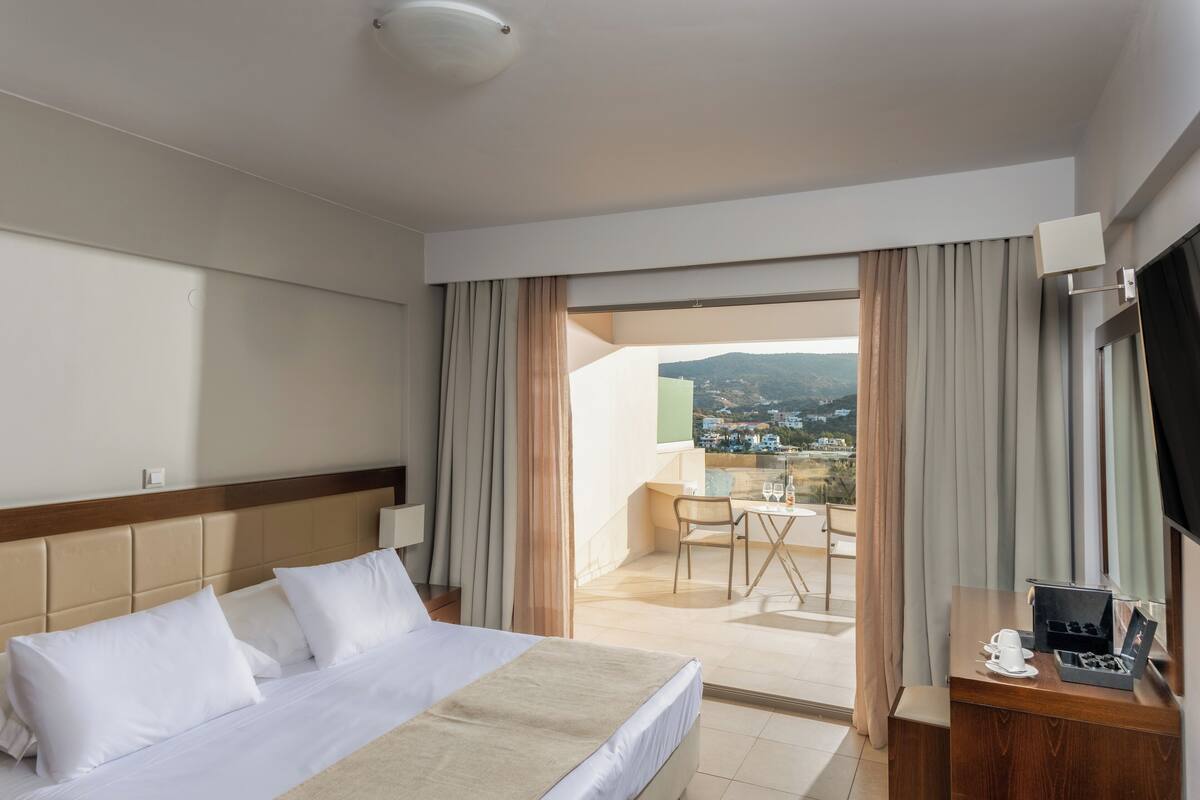 A hotel room with a bed, a desk, a chair, and a view of the outside.