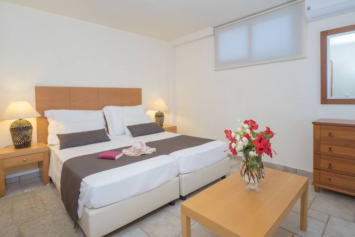 A bedroom with a bed, bedside tables, a nightstand, a wooden dresser, and a vase with flowers.