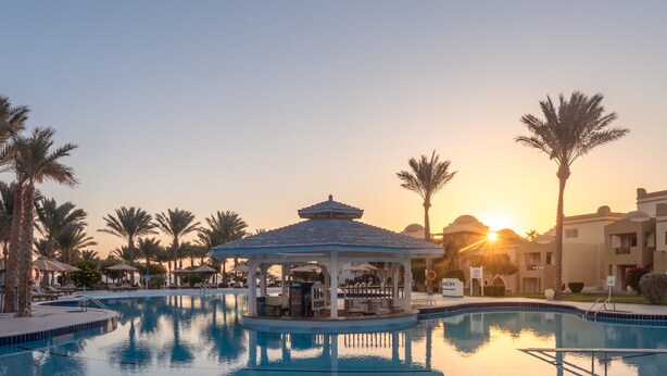 A swimming pool with a gazebo, palm trees, and a sunset in the background. - SRNTY Sea Reef - Ex Serenity Alpha Beach (Makadi Bay)