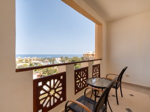 A balcony with a glass table and chairs, overlooking a resort area with palm trees and a view of the sea. - SRNTY Sea Reef - Ex Serenity Alpha Beach (Makadi Bay)