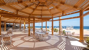 A covered outdoor area with tables and chairs, a view of the beach, and a clear sky. - SRNTY Sea Reef - Ex Serenity Alpha Beach (Makadi Bay)