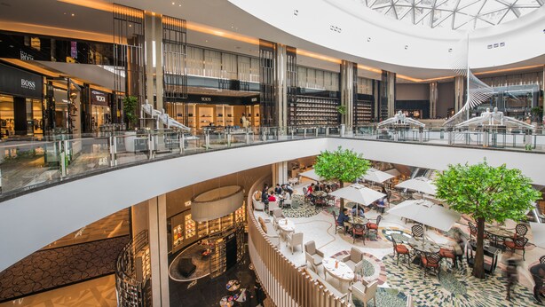 Un centro comercial de varios niveles con tiendas, un atrio central con zonas de descanso y una llamativa escalera en espiral.