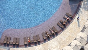 Vista aérea de un área de piscina con sillones de playa y sombrillas.