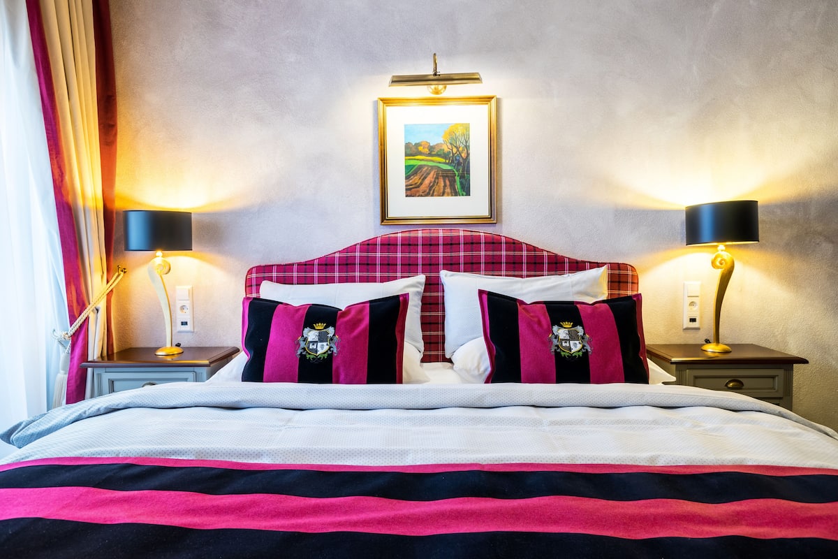 Een hotelkamer met een bed, twee nachtkastjes, een raam met gordijnen en een lijst met een afbeelding aan de muur.
