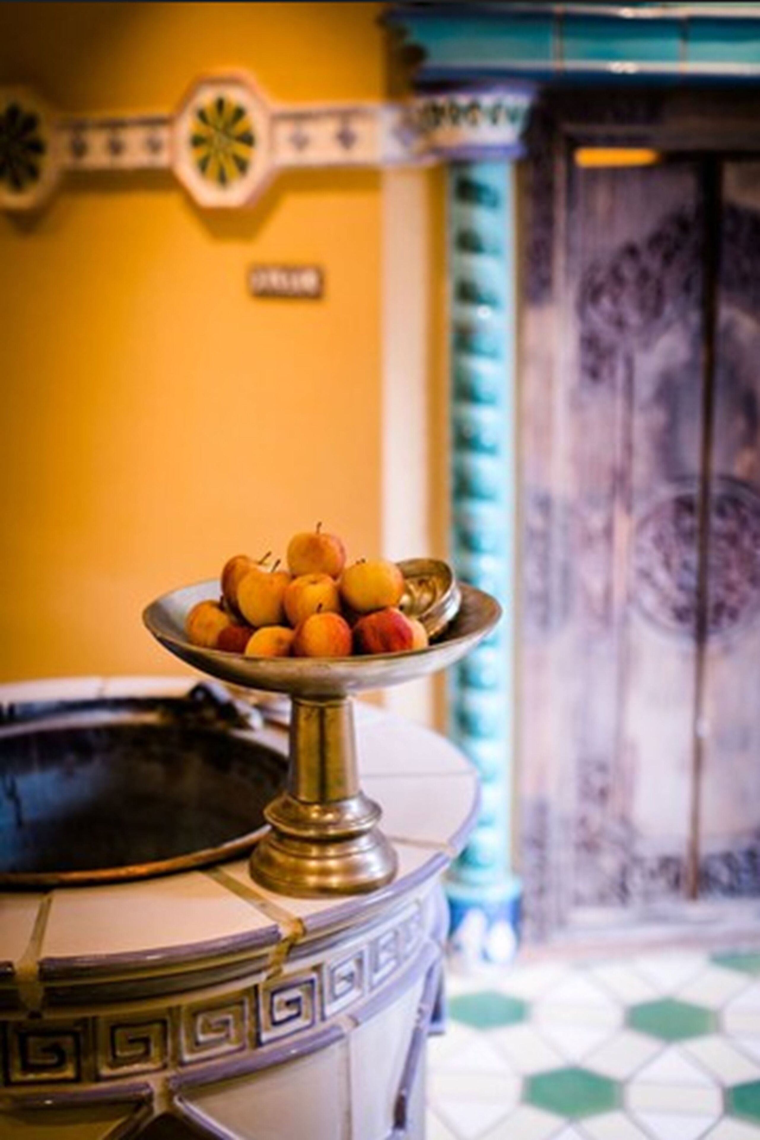 A room with a decorative wall, a tiled floor, and a metal tray with fruits.