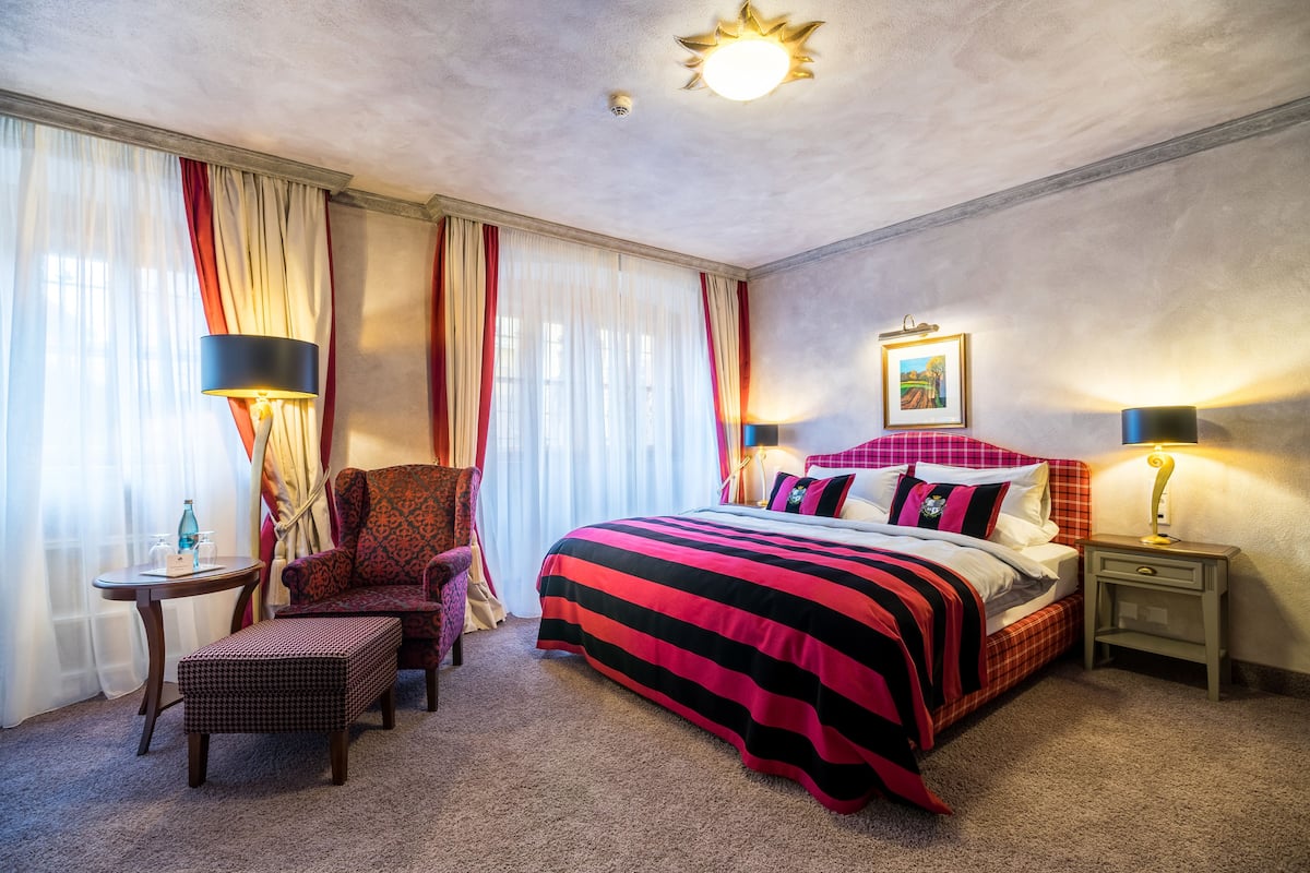 Een hotelkamer met een groot bed, een stoel, een klein tafeltje en een nachtkastje.