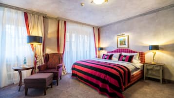 A hotel room with a large bed, a chair, a small table, and a nightstand.