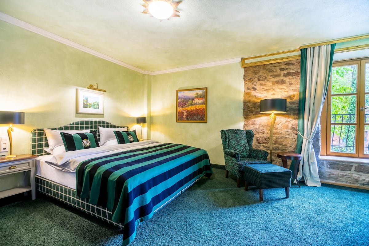 Een hotelkamer met een groot bed, een stoel, een tafeltje en een raam met gordijnen.